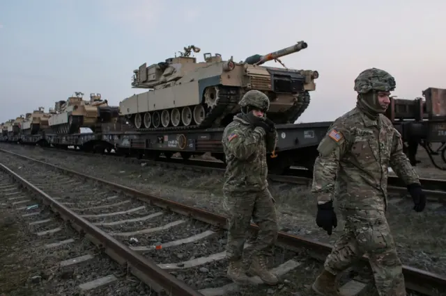 US soldiers walk next to M1 Abrams tanks