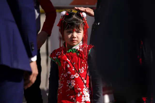 A young girl in her Chinese New Year outfit looks on at law enforcement