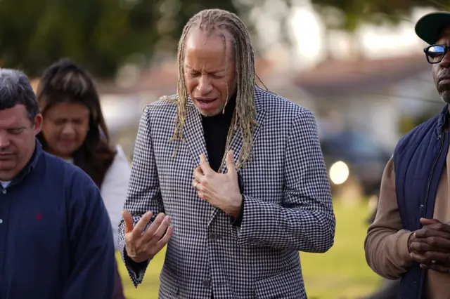 A man says a prayer as members of the community hold a prayer vigil near the scene of a shooting