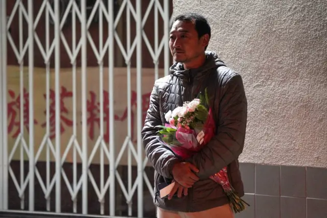 A man holds flowers as he stands near the crime scene