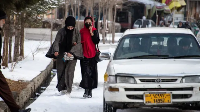 Two women in Kabul walking alongside a car with male passengers