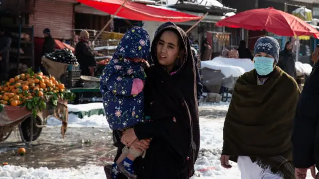 A woman wearing a head covering walks with her child in Kabul