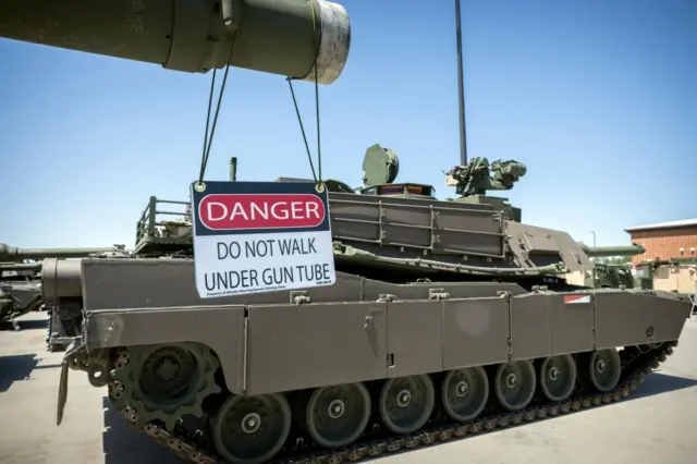 An American-made Abrams tank, with a sign reading: "Danger: do not run under gun tube"