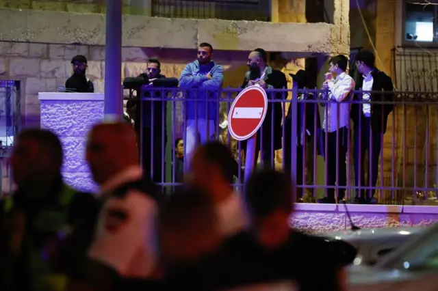 A group of men stand behind railings looking down at the scene of the shooting