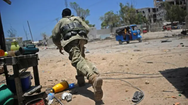 A Somali soldier runs for cover at the scene of two explosions set off near the ministries of public works and labour in Mogadishu on March 23, 2019