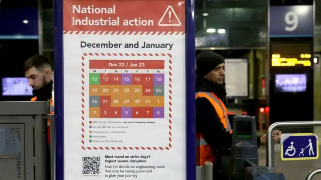 Rail workers stand next to a sign warning passengers of industrial action in December and January