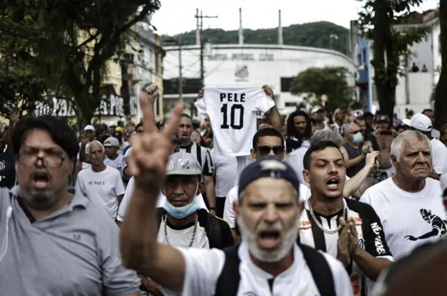 Fans in Santos watch Pele's coffin being carried through the city on a fire truck while holding 'Pele 10' shirts