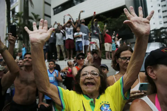 Woman in Brazilian football top smiles for the camera as fans gather in Santos to see Pele's coffin