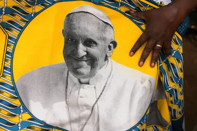 South-Sudanese woman holds a printed fabric with the portrait of Pope Francis