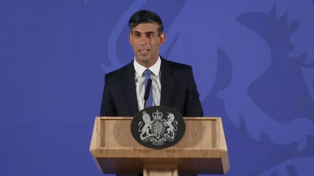 Rishi Sunak, standing in front of a lecturn with the UK government seal, delivering his first speech of 2023