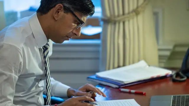 Prime Minister Rishi Sunak writing at a desk