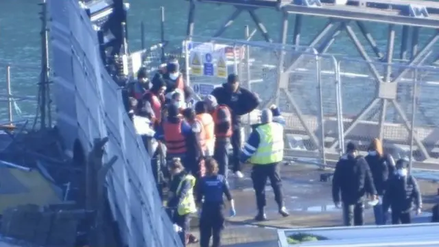 Image shows a group of people standing by the sea in Dover - some wearing life vests