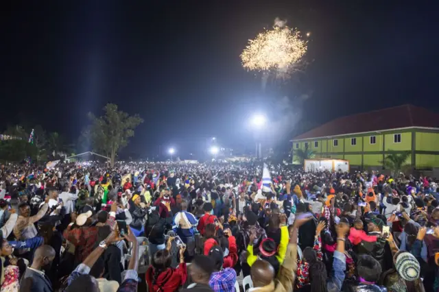 Fireworks light up the sky as people react while they celebrate after counting down to the new year at Miracle Centre Cathedral in Kampala