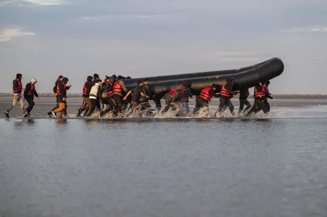 Migrants carry a smuggling boat on their shoulders as they prepare to embark on the beach of Gravelines, near Dunkirk, northern France on October 12, 2022,