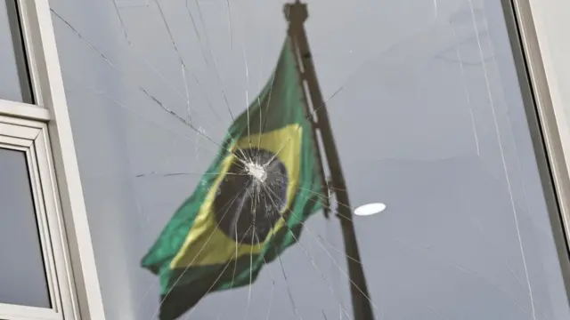 Brazil's flag is reflected on a broken window in the presidential palace in Brasilia