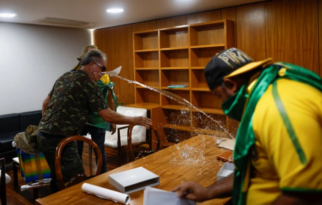 Protesters rummage through paperwork and toss water across an office desk