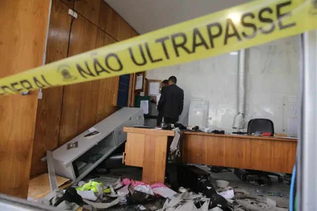 Two men review a destroyed office inside the Planalto Palace