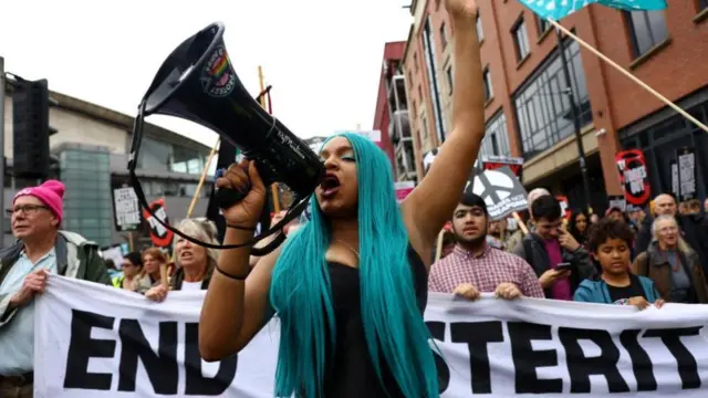 A woman with green hair talks into a megaphone with a crowd behind her