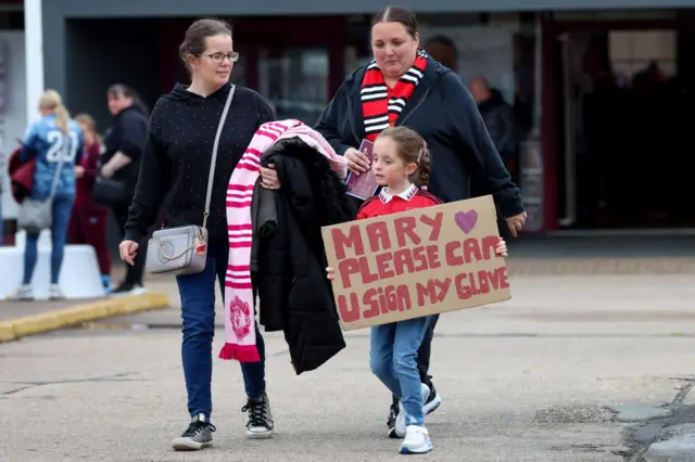 A young fan carries a sign addressed to Mary Earps with her parents in tow.