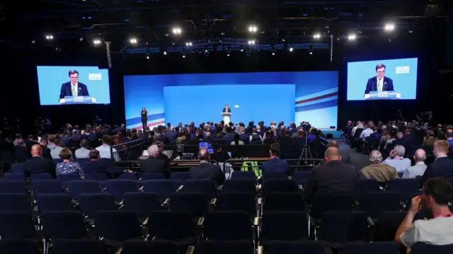 Wide shot of auditorium as Conservative Party chairman Greg Hands speaking on the main stage at the conference