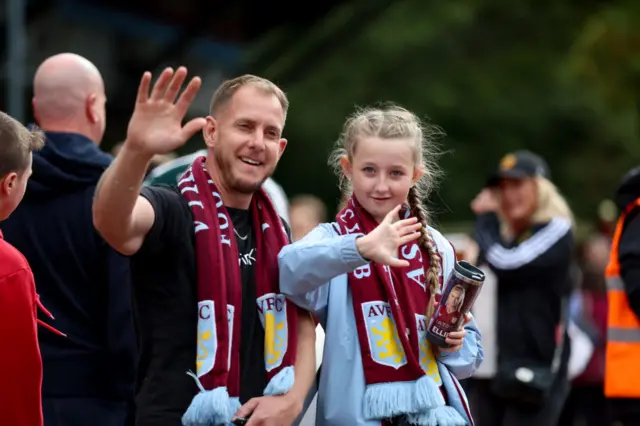 Villa fans wave at the camera adorned with club scarves.