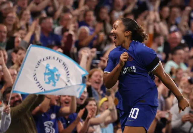 James taps the Chelsea badge on her shirt in front of celebrating fans.