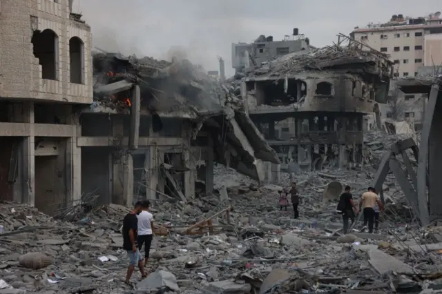 Palestinians walk through debris of a bombed building