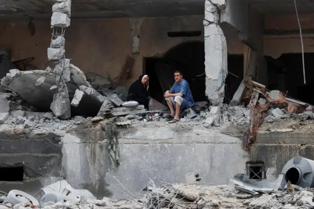 Palestinians sit among rubbles of a damaged residential building