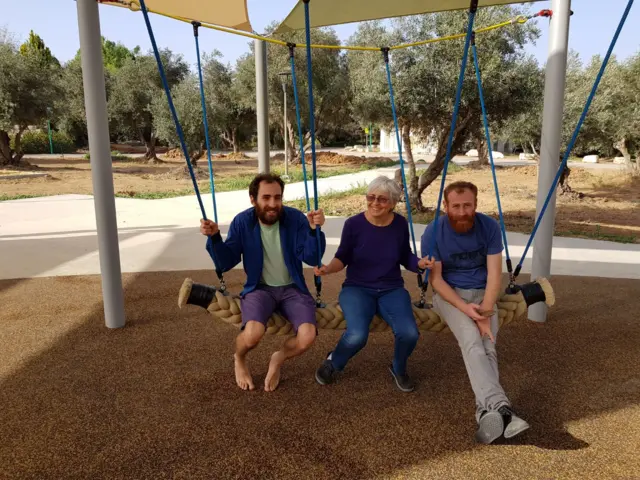 Two men sit on a swing with their mother in the middle
