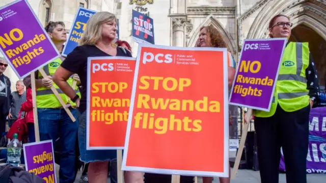 Protesters in the UK hold placards opposed to the Rwanda refugee scheme during the demonstration.