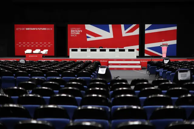 A stage with empty seats in front of it. British flags as stage background.