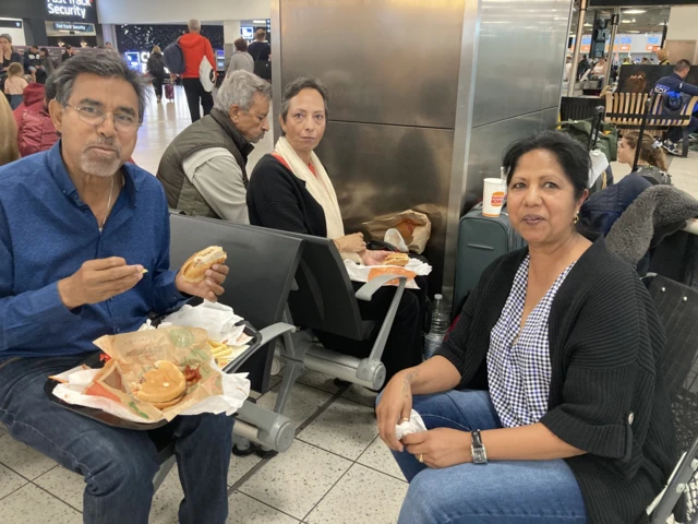 Gian and Jareena Sarabatta (foreground) with her aunt and uncle in the background. They are eating burgers in the waiting area of the terminal.