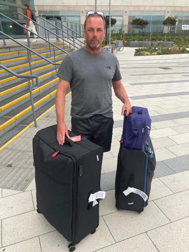 Justin Harris standing at an airport with his suitcases.