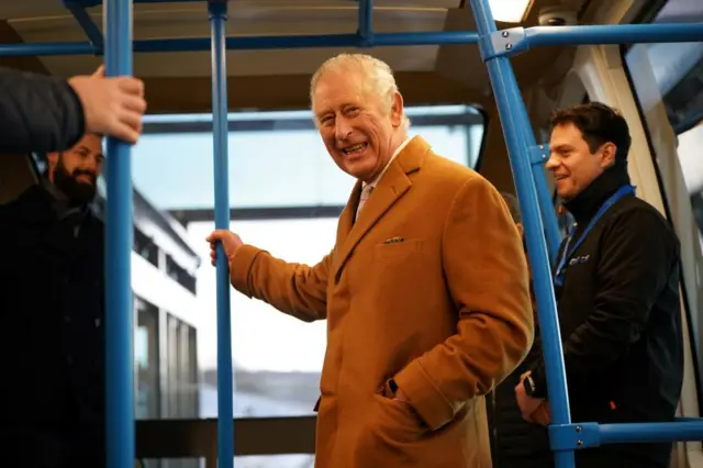 King Charles smiling as he rides a Dart train in December 2022