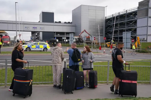 Passengers with suitcases look at the burned-out carparkPassengers with suitcases look at the burned-out carpark