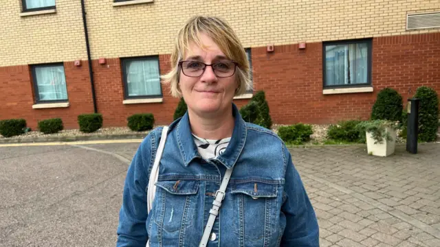 Helen Hodson. She is standing outside a hotel wearing glasses, a white top and denim jacket.