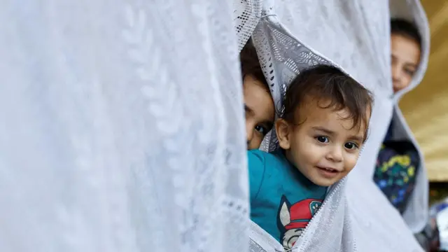 Palestinian children poke their heads out of makeshift shelters at the hospital