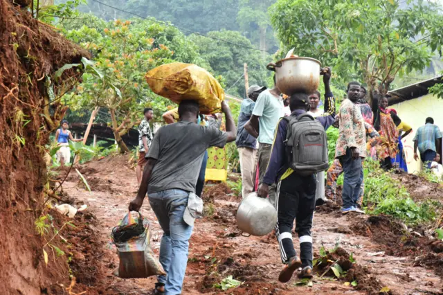 People carry objects following a landslide caused by torrential rains in Mbankolo district of Yaounde, the capital of the Central African country Cameroon, on October 10, 2023.