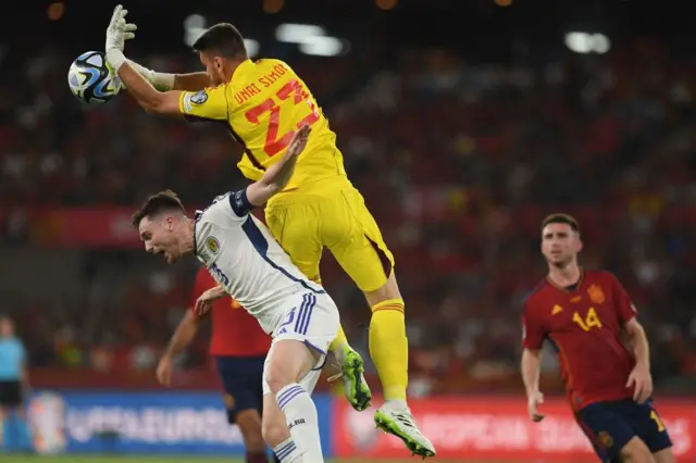 Unai Simon jumps for the ball next to Scotland's defender #03 Andrew Robertson during the EURO 2024 first round group A qualifying football match between Spain and Scotland at the La Cartuja stadium in Seville