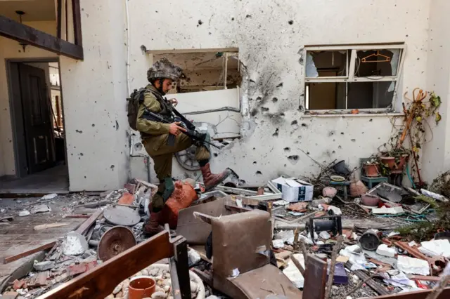 An Israeli soldier steps over personal belongings near a home, following a deadly attack by Hamas gunmen on Kibbutz Be'eri in southern Israel