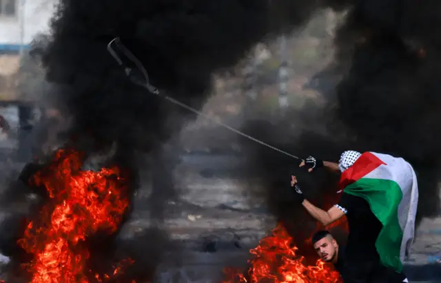 A Palestinian uses a slingshot during clashes with Israeli soldiers at the north entrance of the Palestinian city of Ramallah