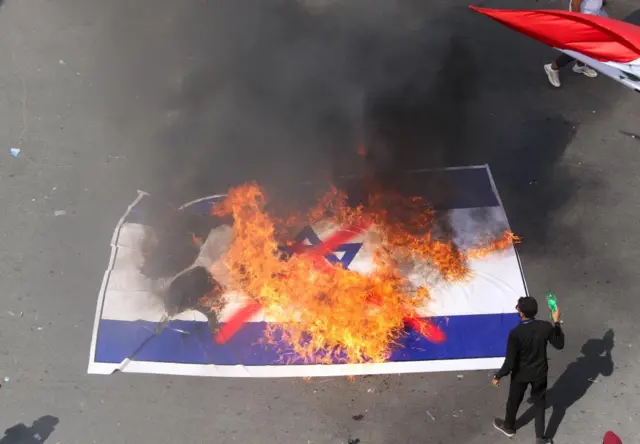 A protester setting an Israeli flag lying on the ground alight