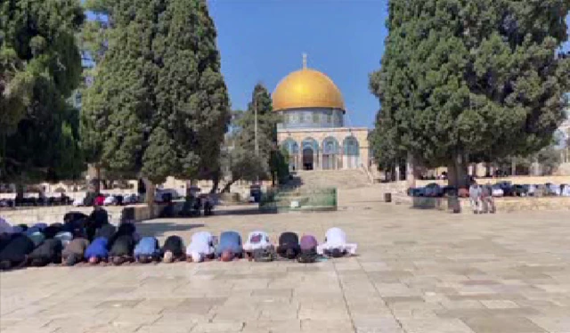 Muslims praying with the Dome of the Rock behind them.