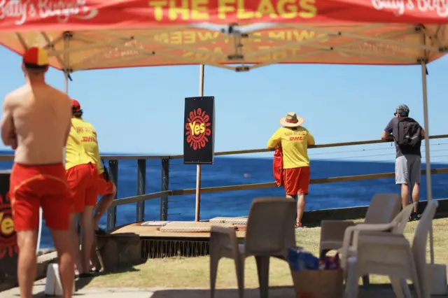 Surf lifesavers keep watch at a Sydney beach next to a Yes sign