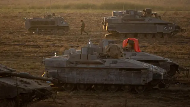 An Israeli soldier walks next to armored vehicles sitting in an area along the border with Gaza, southern Israel