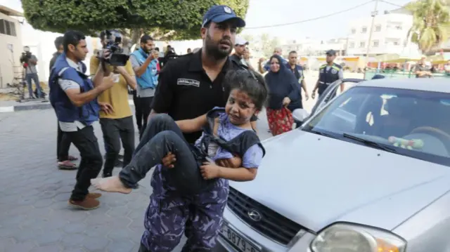 A police officer carries a child into a hospital following an Israeli attack on Deir Al Balah in central Gaza