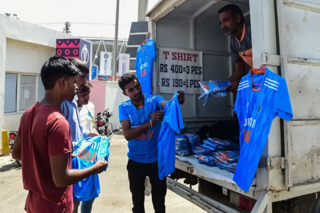 A vendor (C) sells Indian cricket jerseys to customers outside the Narendra Modi Stadium in Ahmedabad on October 10, 2023.