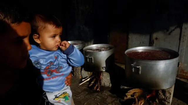 Children watch as food is cooked on firewood amid shortages of fuel and gas to provide food for Palestinians who fled their houses amid Israeli strikes in Khan Younis