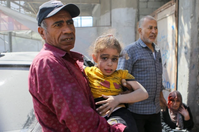 A Palestinian man carries a girl hurt by Israeli strikes in Gaza City