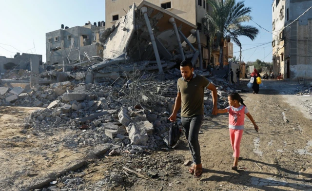 Palestinians walk by the site of Israeli strikes on houses in Khan Younis in the southern Gaza Strip